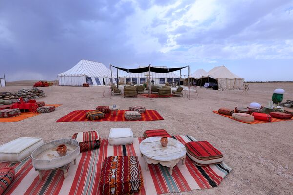 Day camp in Agafay Desert with colourful blankets, floor cushions and wooden tables.