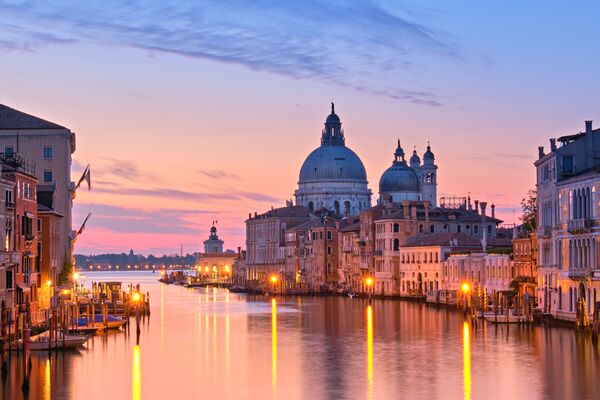 Romantic Venice at dawn, sunrise. Cityscape image of Grand Canal in Venice, with Santa Maria della Salute Basilica reflected in calm sea. Street lights reflected in calm water.